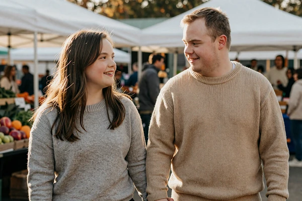 Mia and Daniel, a Down syndrome couple, holding hands at a farmers market - down syndrome couples success story