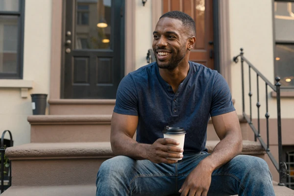 Marcus, a man with temporal lobe epilepsy, laughing on a Brooklyn stoop with coffee - late-diagnosed epilepsy dating story