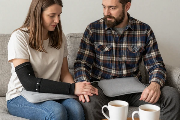 Kaci and Collin, a chronic illness couple, holding hands on their cozy couch with tea and a heating pad - finding love with a disability